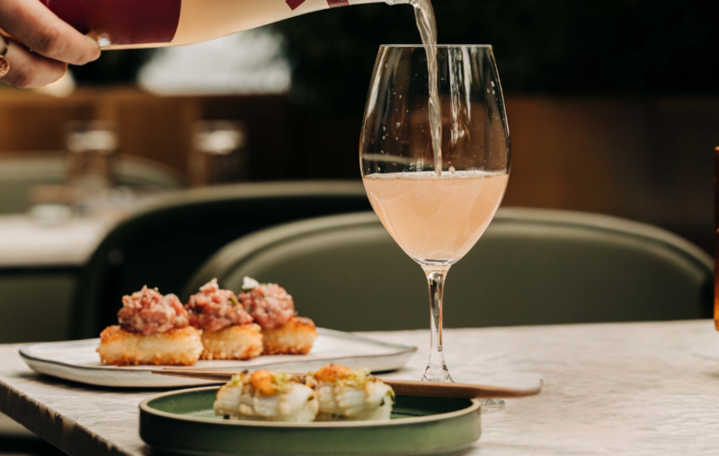 A glass of rose sake being poured at Sushi-san Lincoln Park with Spicy Tuna Crispy Rice and nigiri