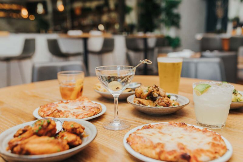Happy hour spread with pizzas, wings, and cocktails.