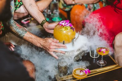 large tropical cocktail being placed on a tray with smoke drifting from it