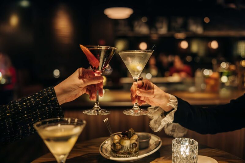 Two hands toasting with a Martini and Martinez cocktails at Gus' Sip & Dip