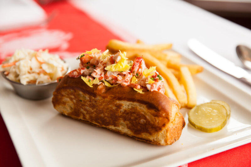 Shaw's Lobster Roll on a plate with french fries, slaw and pickles on the side
