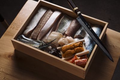 overhead photo of a wooden box holding a variety of fish with a knife resting on its corner