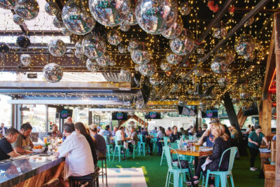 main seating area for happy camper las vegas. bar seating to the right and tables to the left. the ceiling is decorated with mirror balls and Christmas Lights