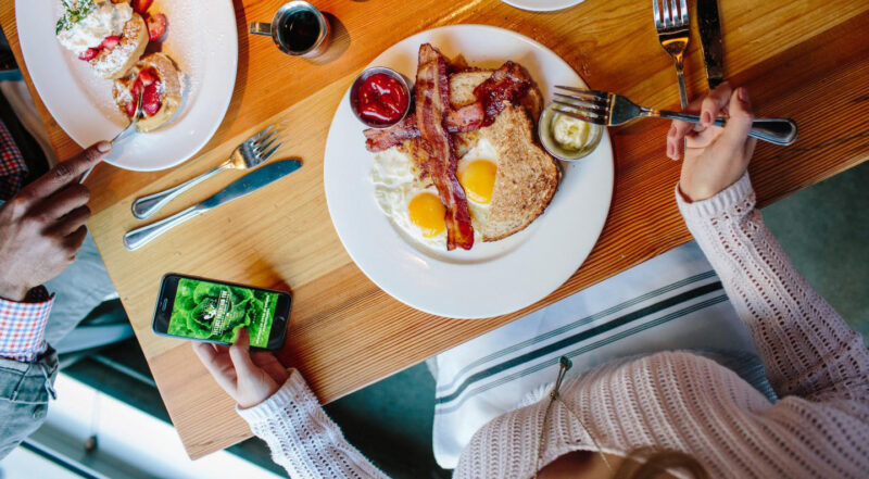 Brunch table with woman looking at her LettuceEats App on her phone