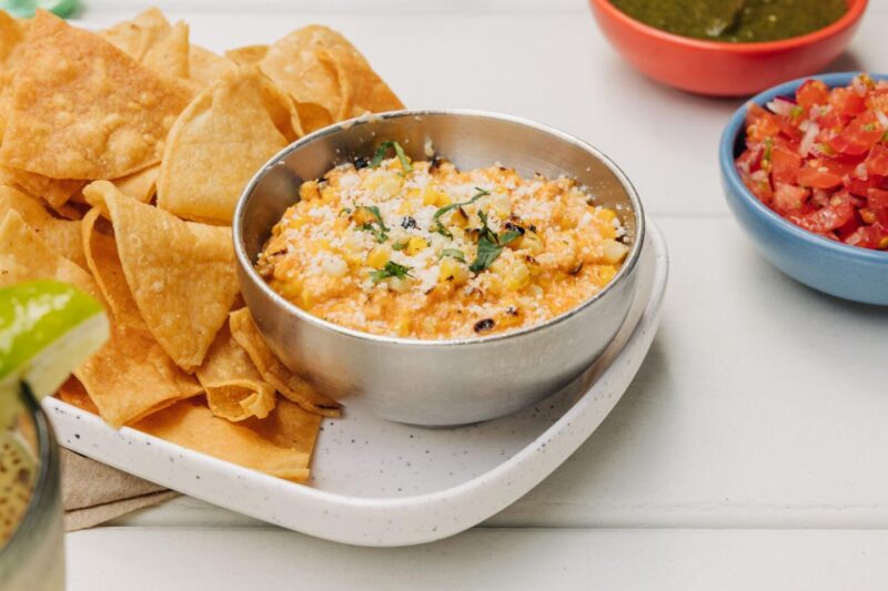 Bowl of Corn Fundito with tortilla chips and other condiments on the side