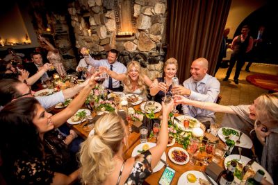 Exuberant wedding party, seated around the bride and groom at the table, raising their glasses in a toast