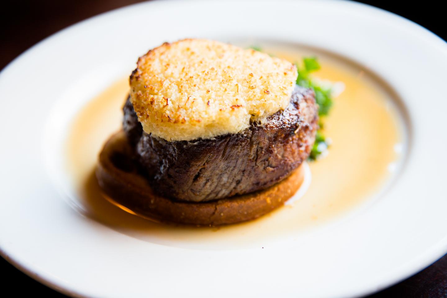 Horseradish crusted filet sitting in its jus on a white plate