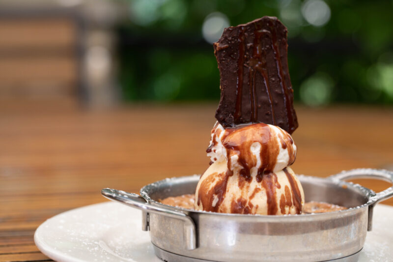 chocolate chip cookie in silver skillet woth ice cream on top with chocolate sauce, and a piece of chocolate  on top.