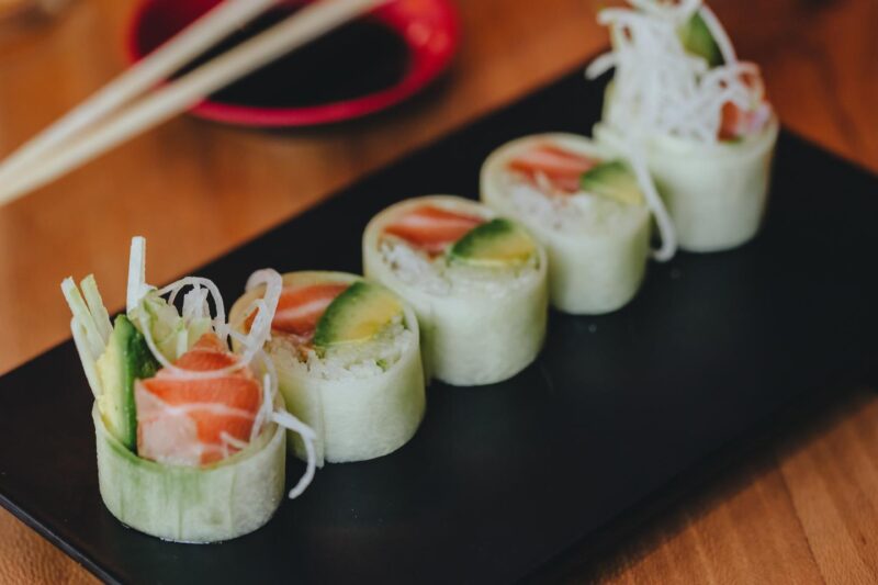 Cucumber-wrapped sushi from sushi-san set on a black sushi tray and resting on a wooden background