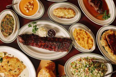 Several plates of food such as ribs, mac and cheese, a baked potato, soup and salad