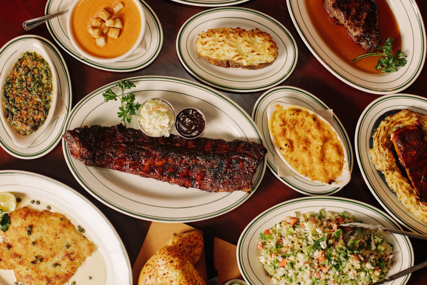 Several plates of food such as ribs, mac and cheese, a baked potato, soup and salad
