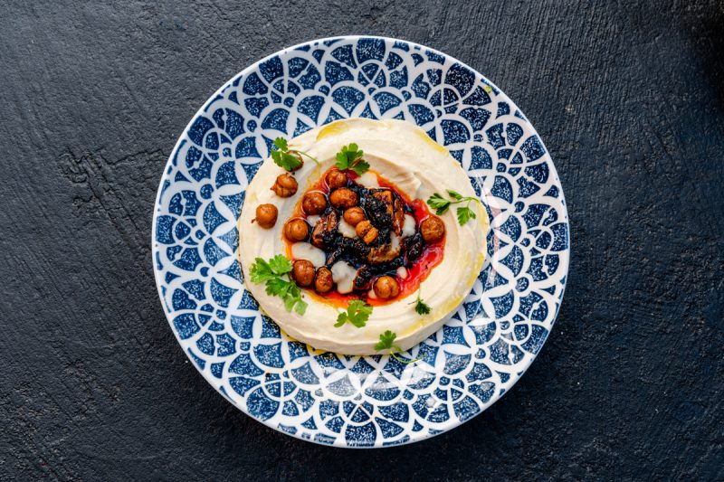 overhead photo of garlic hummus toped with chickpeas served on a blue and white plate