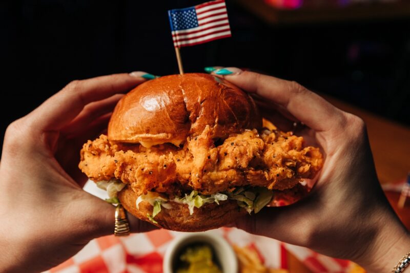 Fried chicken sandwich with an American flag toothpick sticking out of the stop. 