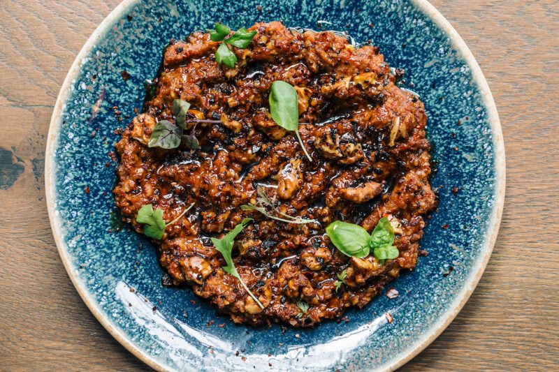 Close up on a plate of smoky Muhammara from Aba, with fresh herbs as garnish