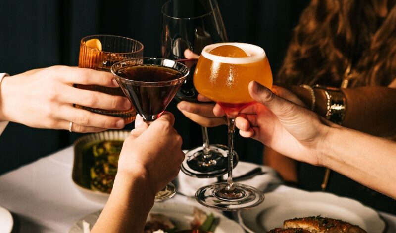 Four hands holding cocktails and wine up in a toast at Tre Dita