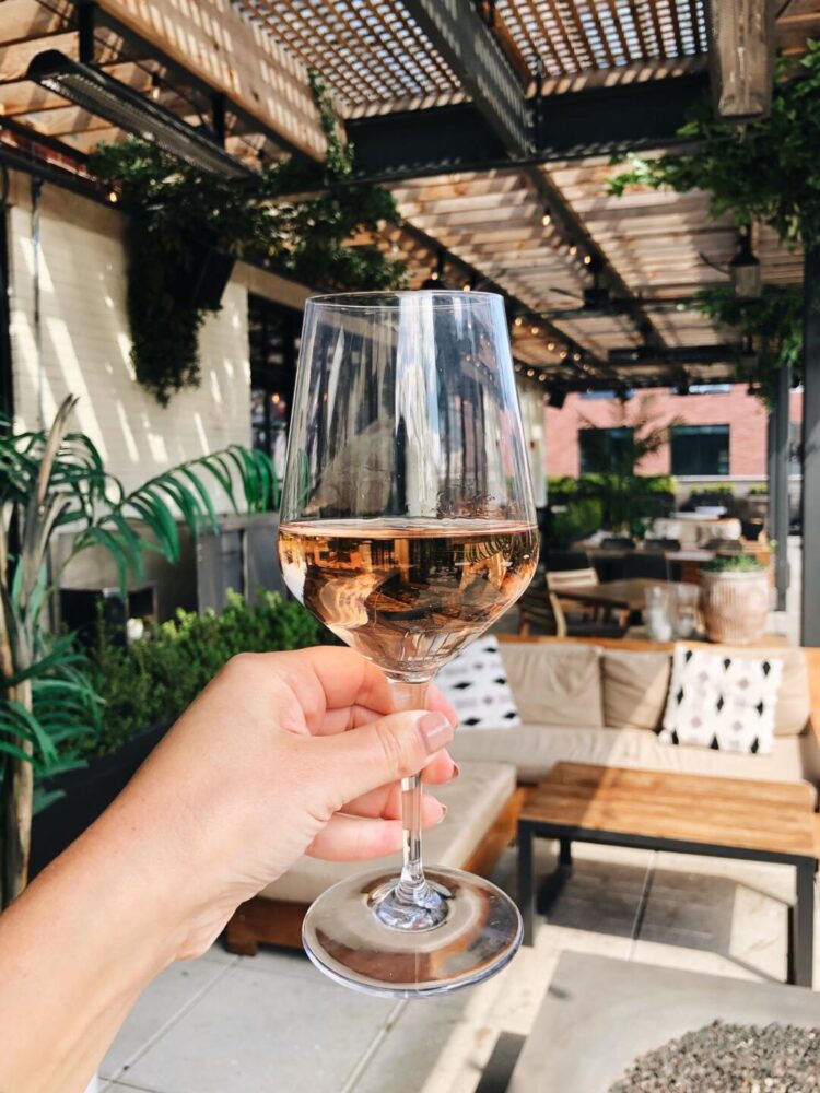 Hand holding a glass of rose with the Aba patio area showing in the background