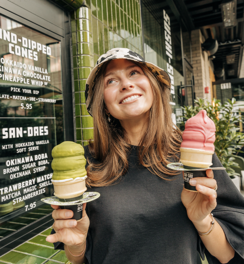 A girl holding up two soft serve cones dipped in pink and green flavors