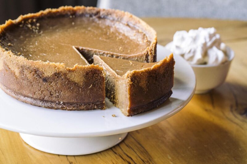 Beatrix Whole Caramel Pie resting on a white pie stand with a bowl of whipped cream next to it