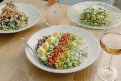 Popular salads including cobb salad and shaved brussels sprouts salad. Glass of rosé on the side.