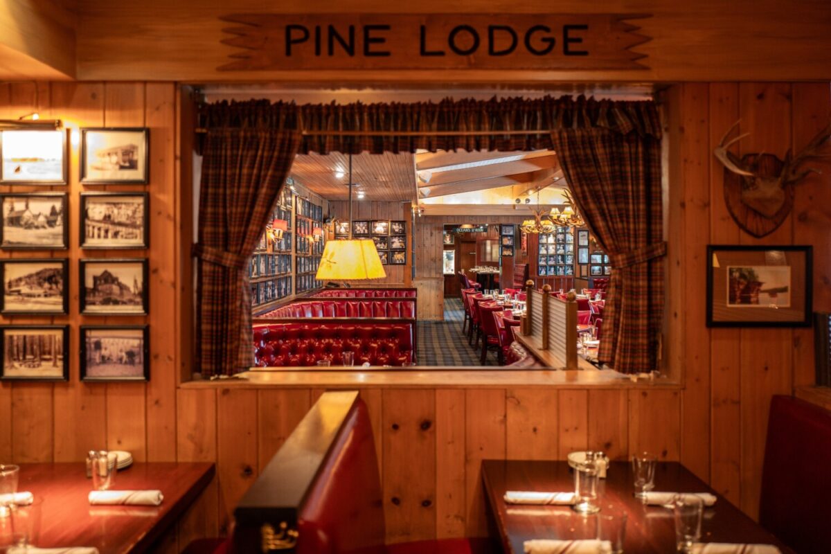 A restaurant booth in a wood paneled room with a sign reading Pine Lodge