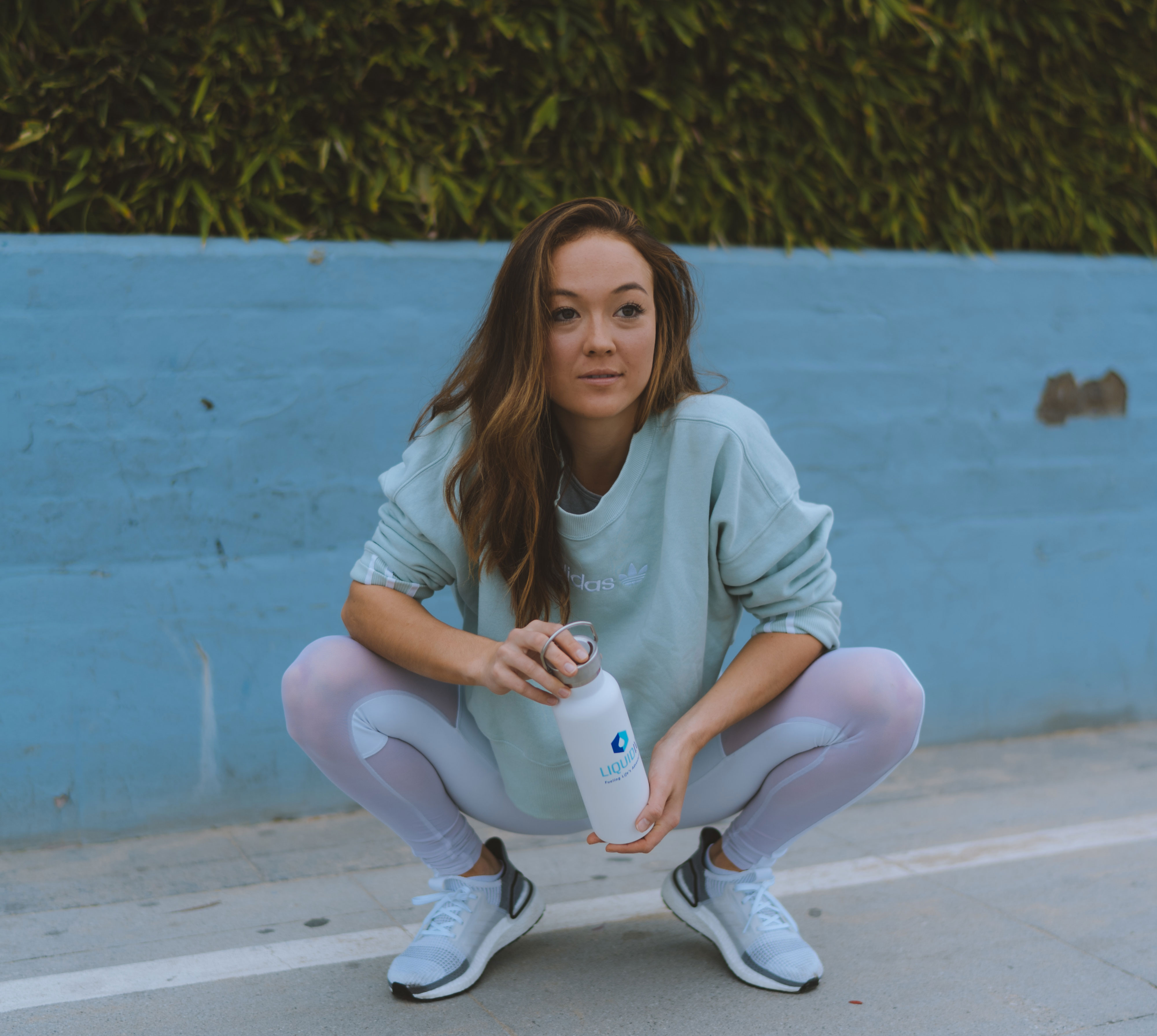 Model on set in squat position holding Liquid I.V. water bottle