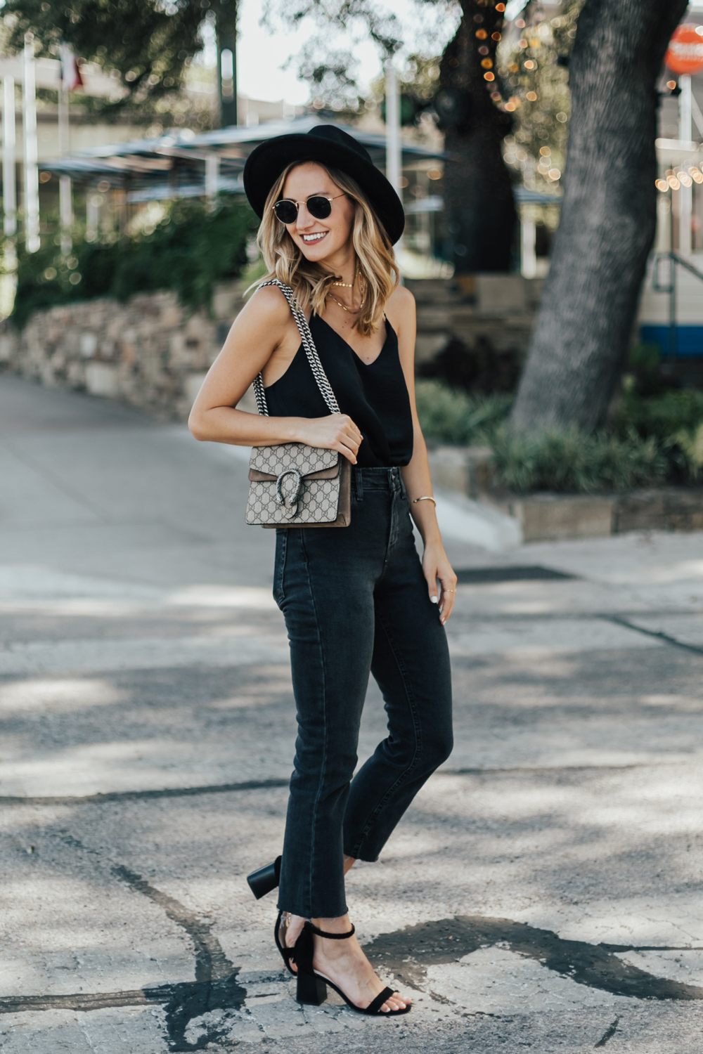 Young stylish woman wearing black cami silk top, blue cropped denim jeans,  black high heel sandals