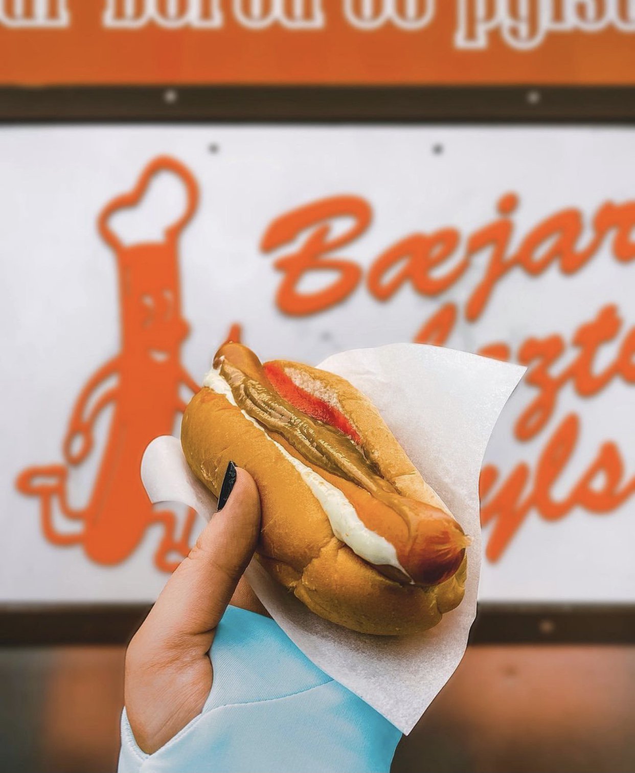 image of hand holding a hotdog in front of a hotdog stand