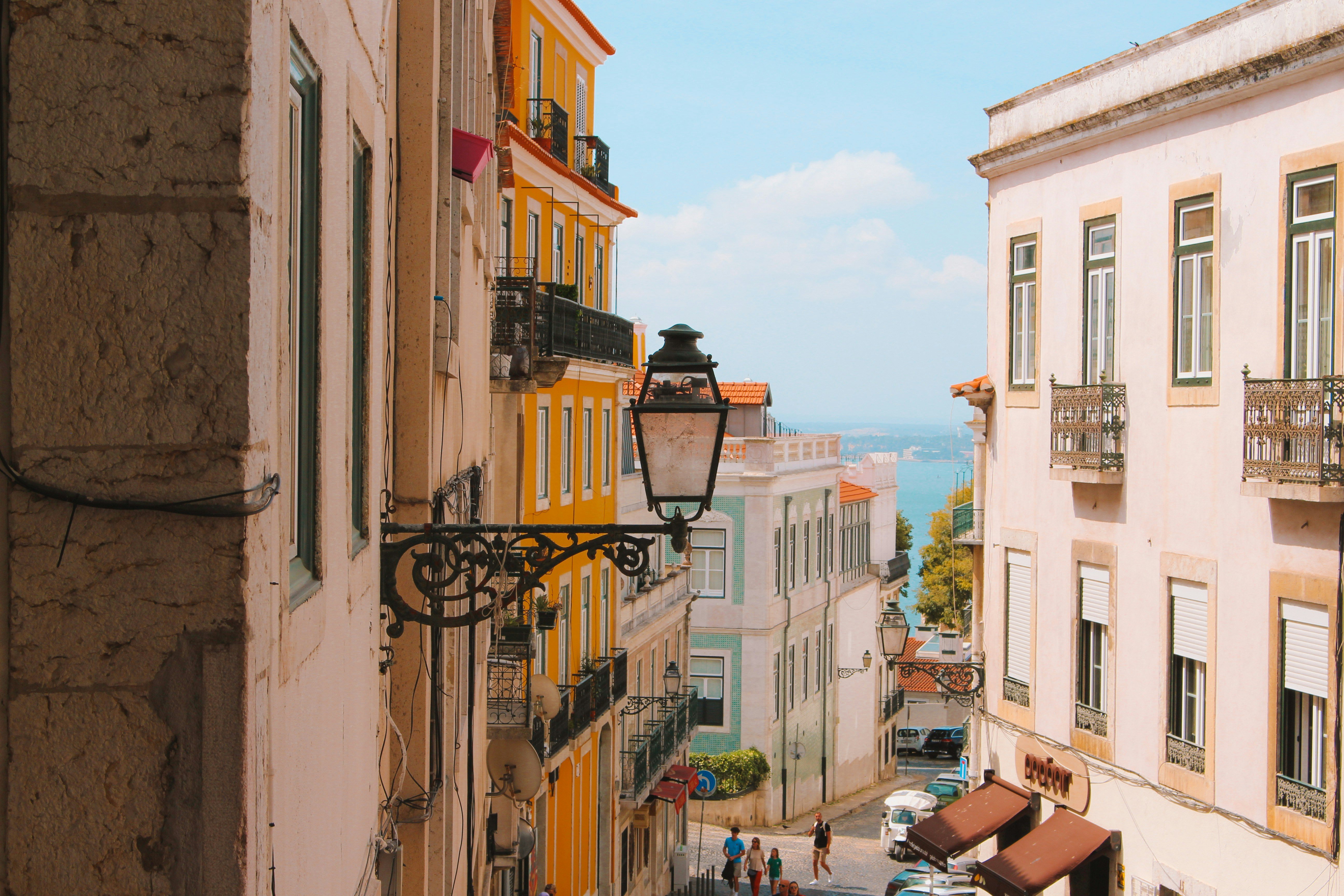 Scenic view of Lisbon city with colorful buildings, terracotta rooftops, and the Tagus River in the background under a clear sky.