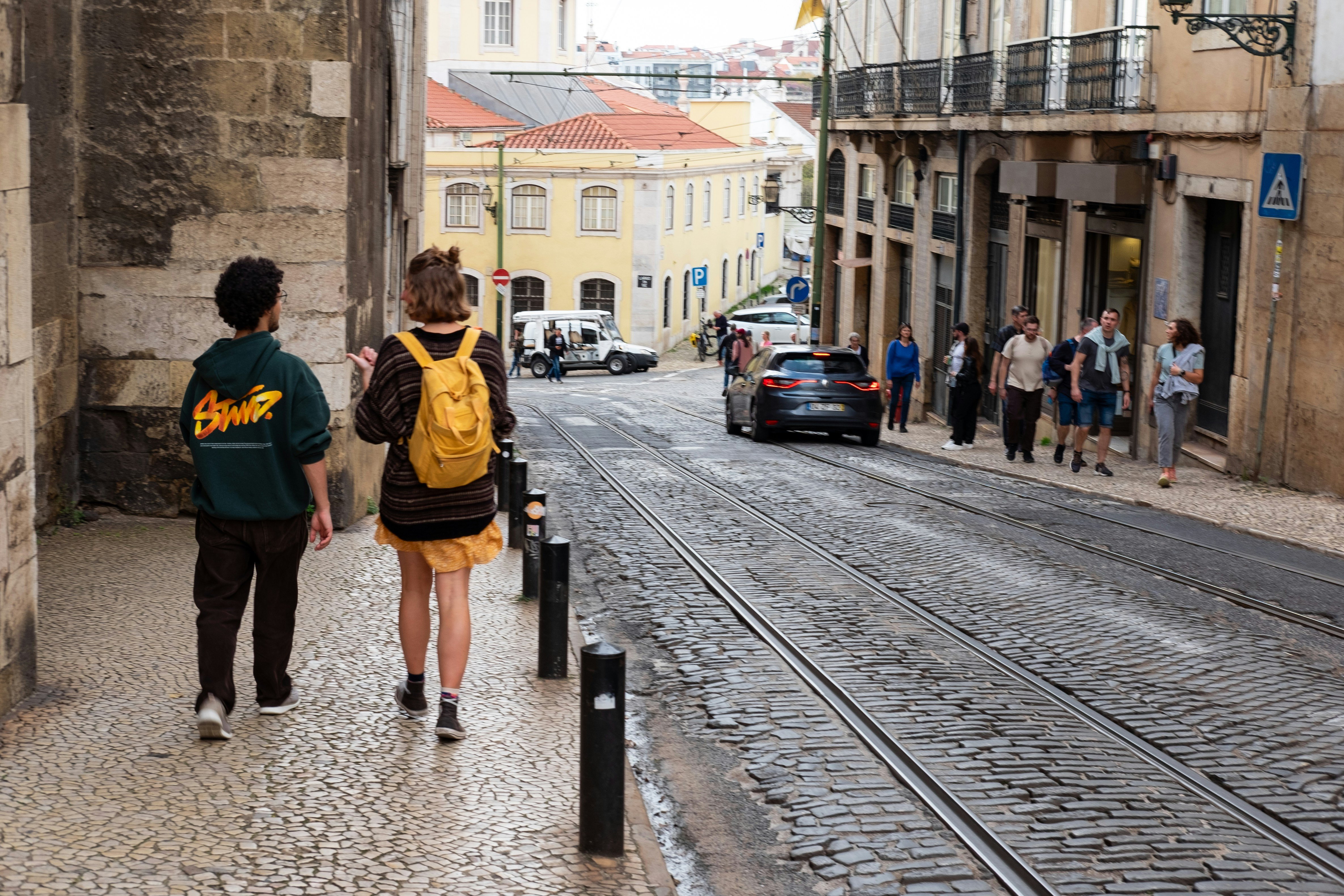 People walking through the cobblestone streets of Lisbon, Portugal, with colorful buildings and sunlight in the background.