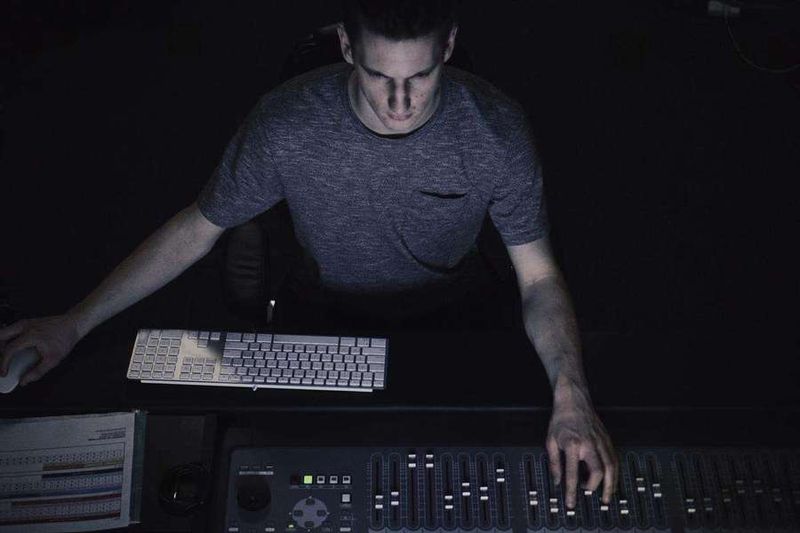 Comment devenir DJ : un homme dans l'obscurité travaille sur une table de mixage et son ordinateur.