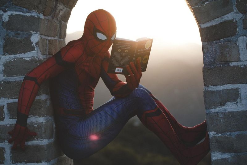 Une personne déguisée en Spiderman lit un livre.