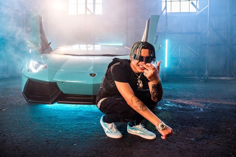 Un rappeur devant une voiture de sport.