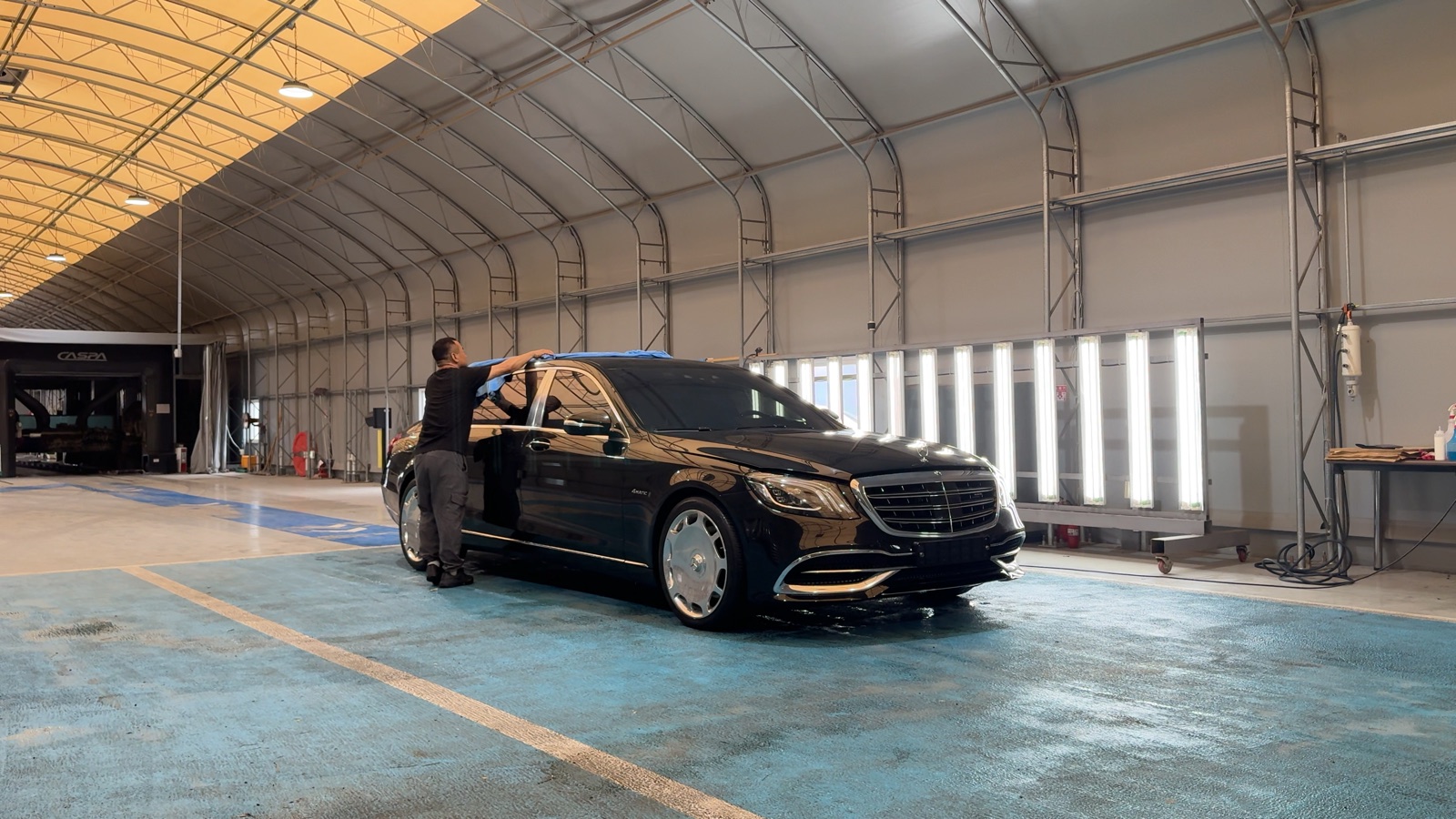 An LMN staff member drying a freshly washed black Mercedes-Maybach in the wide bay of the LMN facility in Korea.
