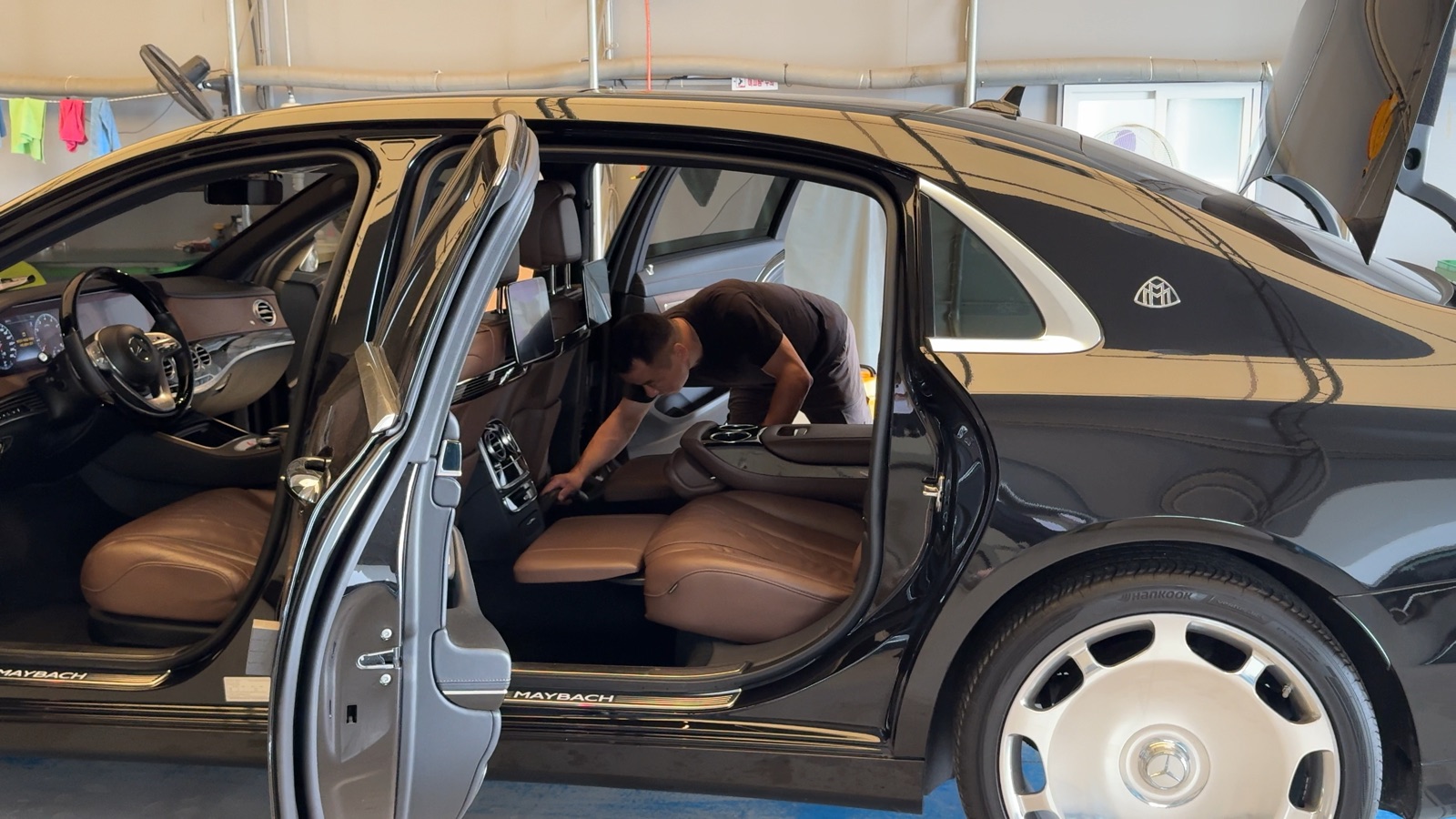 An LMN staff member cleaning the rear cabin of a secured black Mercedes-Maybach, doors open, at the LMN facility.