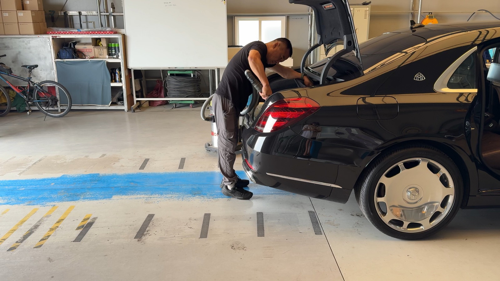 An LMN staff member vacuuming the open trunk of a secured black Mercedes-Maybach at the LMN facility.