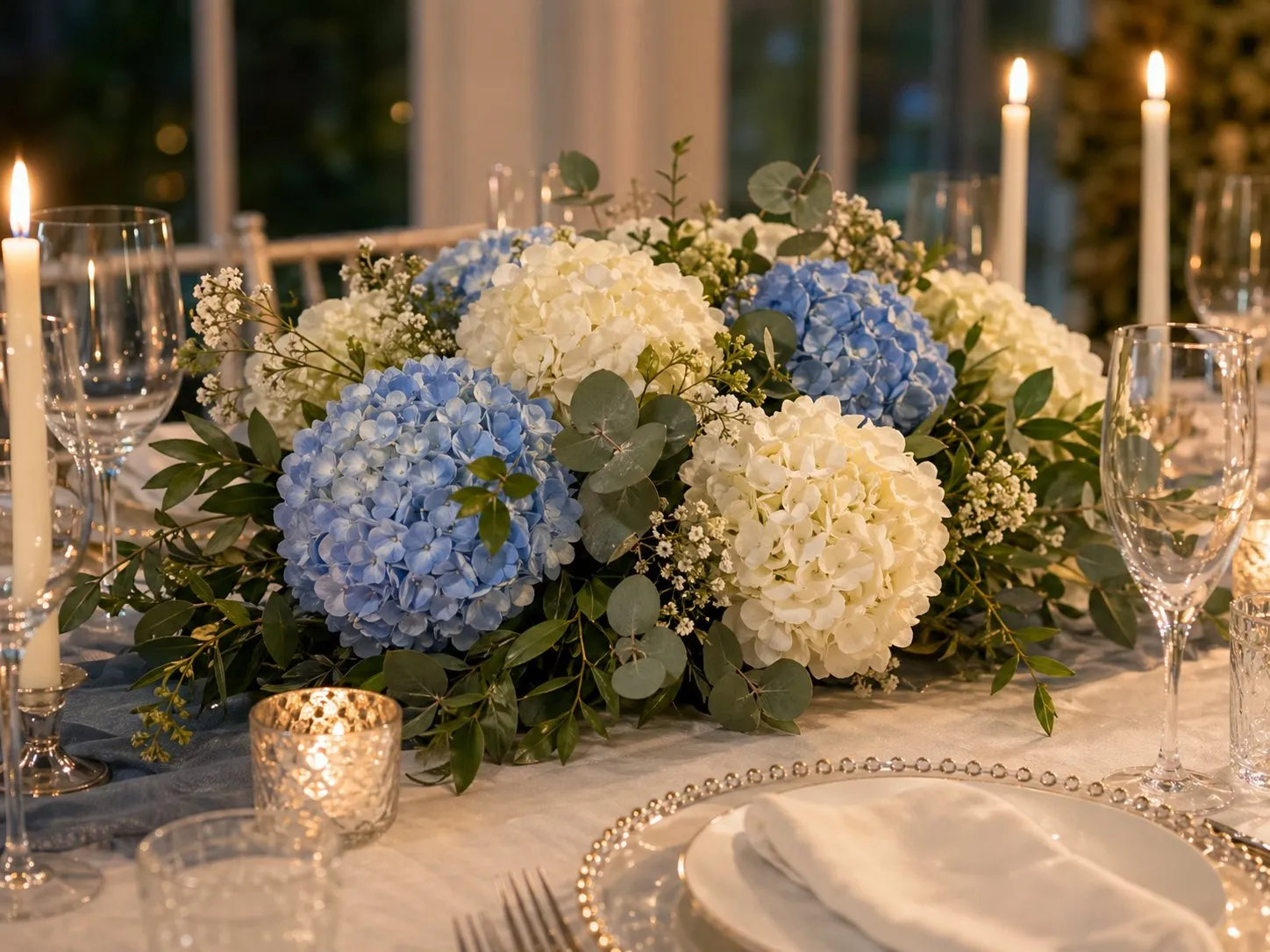White and blue hydrangeas arranged on an elegant table with candles