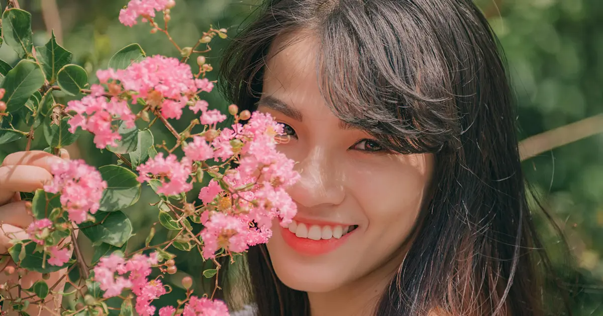 A photo of a beautiful Asian woman posing behind some flowers