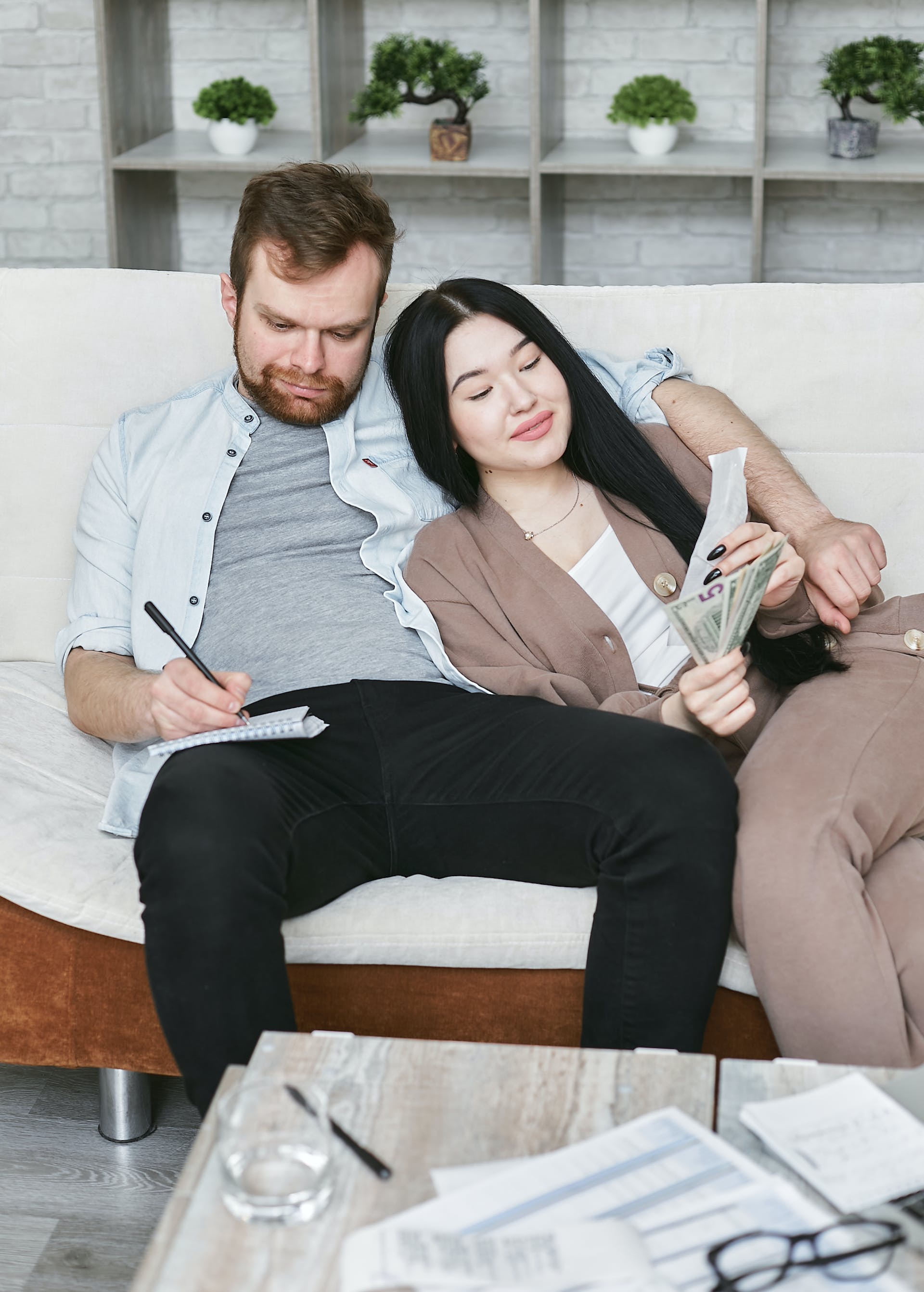 A couple sitting on a couch while making notes about money
