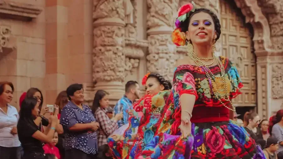 A Mexican woman wearing colorful clothes with people in the background