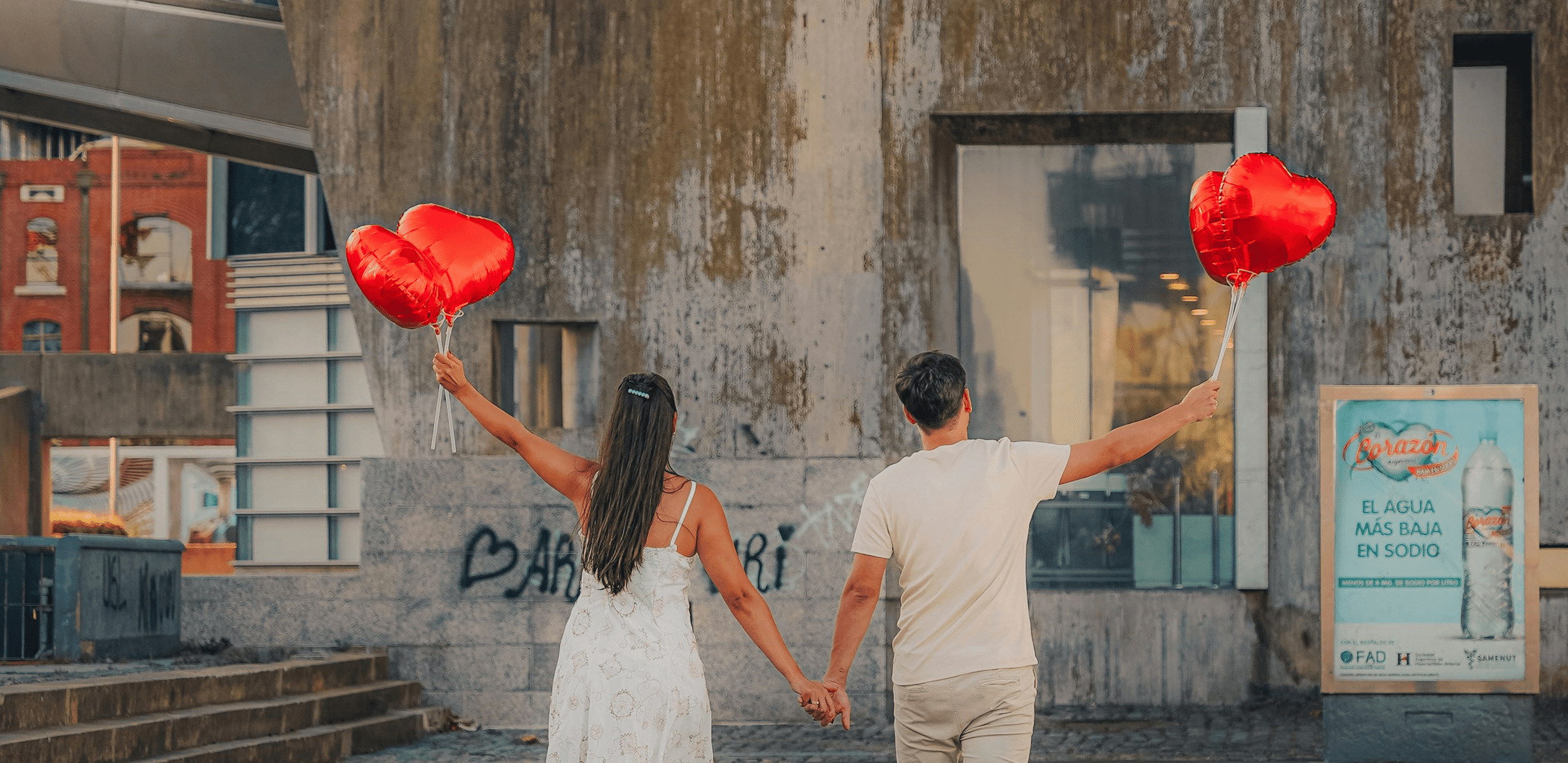 A couple holding hands and carrying heart balloons up in the air