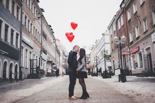 A photo of an online dating couple holding up heart shaped cardboards against their faces.
