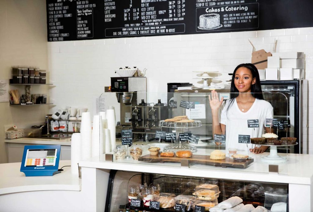 Waving woman behind a counter at a coffee shop.