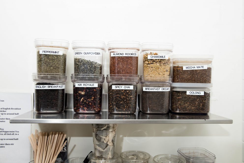 Clear containers of loose leaf tea stacked on a metal shelf.