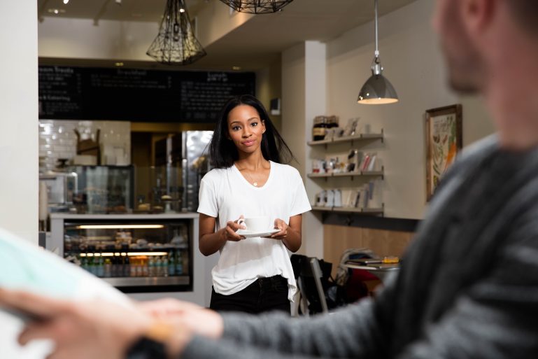 A coffee shop employee carrying a cup of coffee to a customer.