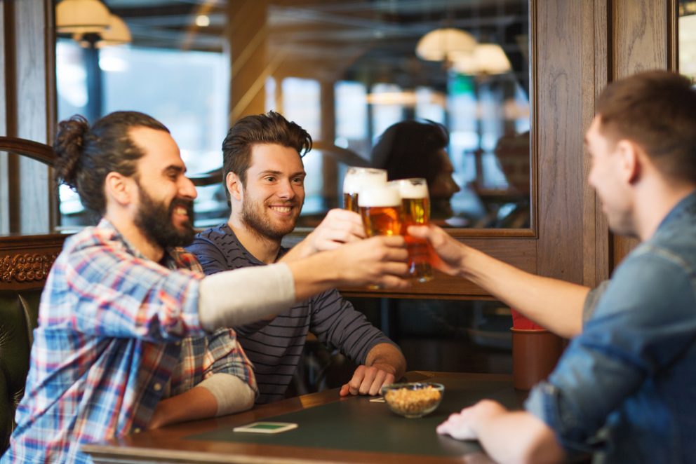 Bearded men toasting with beer at a bar table.