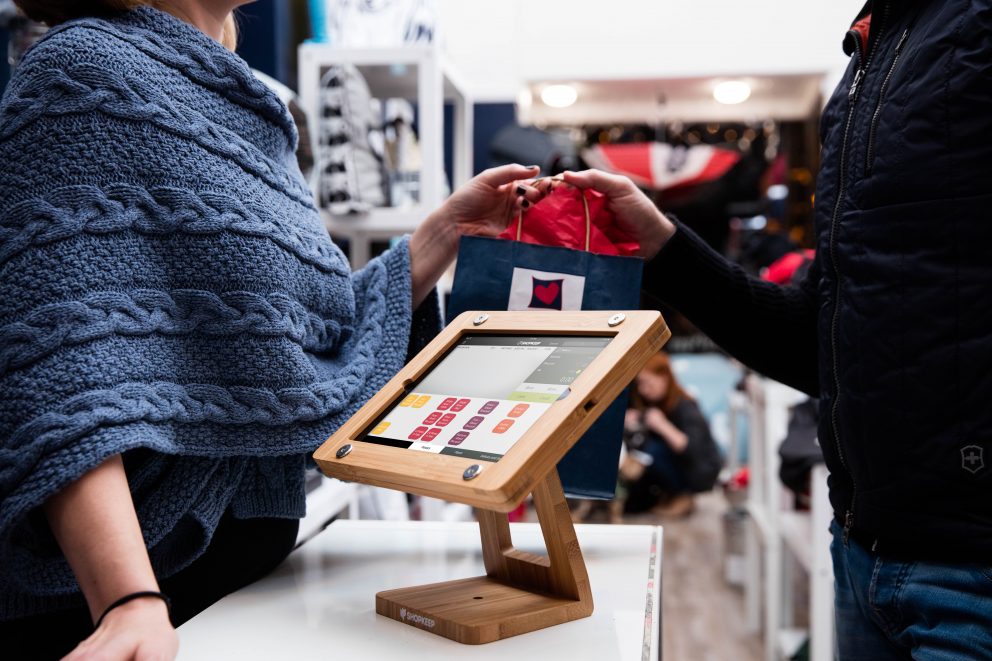 An employee handing a customer a bag with a ShopKeep terminal in the foreground.