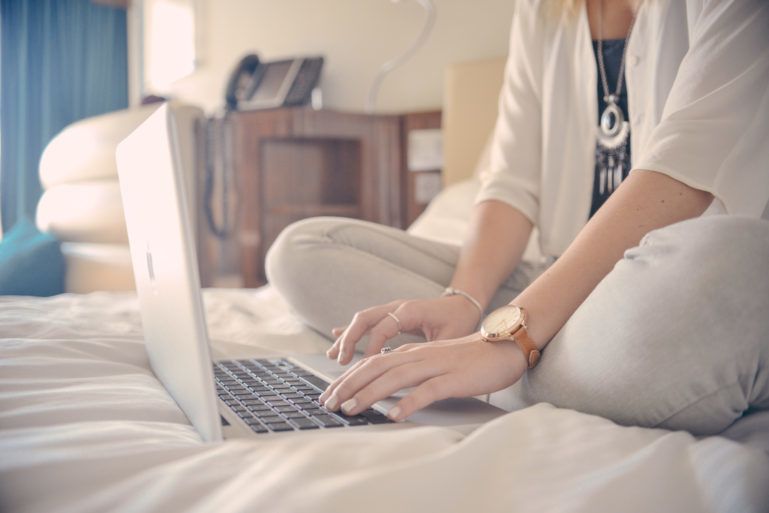 woman using laptop on her bed - advantages and disadvantages of ecommerce