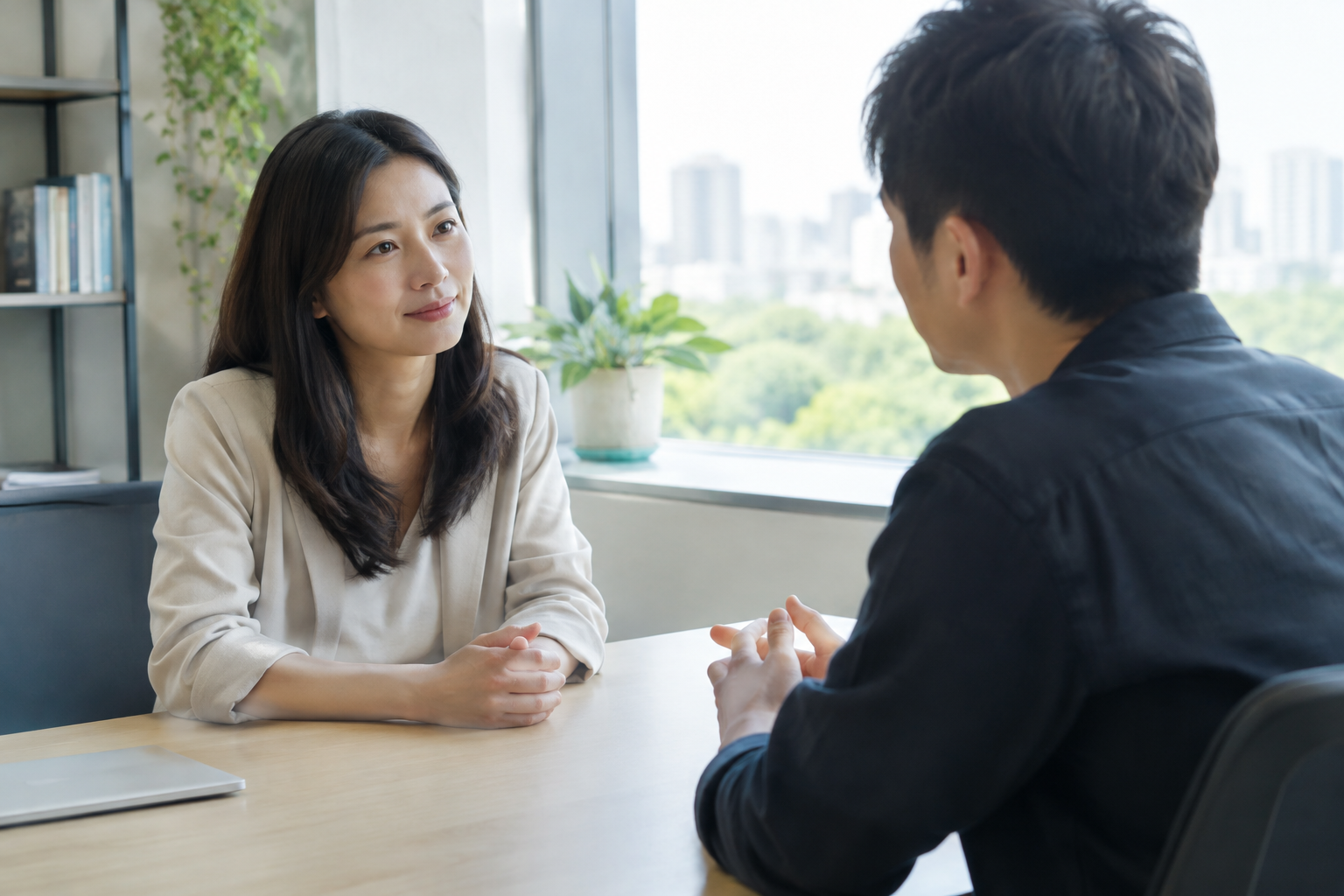主管與團隊成員在安靜明亮的辦公空間中進行一對一對話,東亞人物坐姿開放、專注傾聽,桌面簡潔,窗邊自然光灑入,氛圍支持且信任,真實攝影風格,不含任何文字