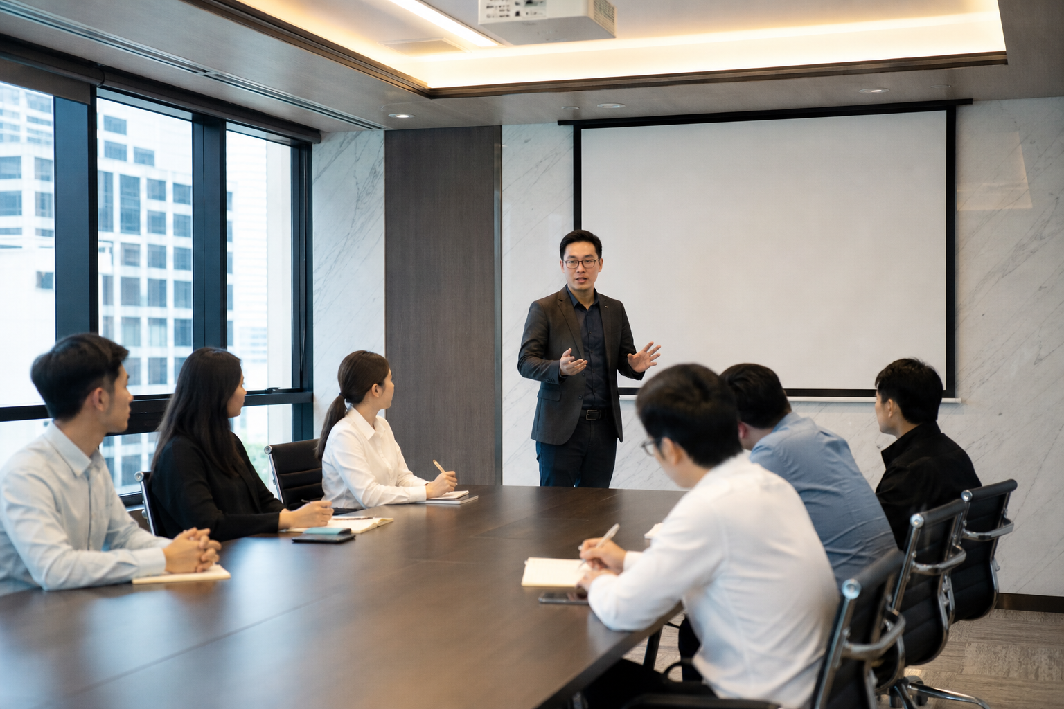企業會議室內的法遵教育訓練場景,中景構圖,一位講師站在投影幕前說明法規內容,數位東亞主管與員工坐在會議桌旁專注聆聽並做筆記,室內明亮自然光與柔和頂燈交錯,現代辦公空間整潔有序,整體氛圍理性、專注且略帶正式感,真實攝影風格,不含任何文字