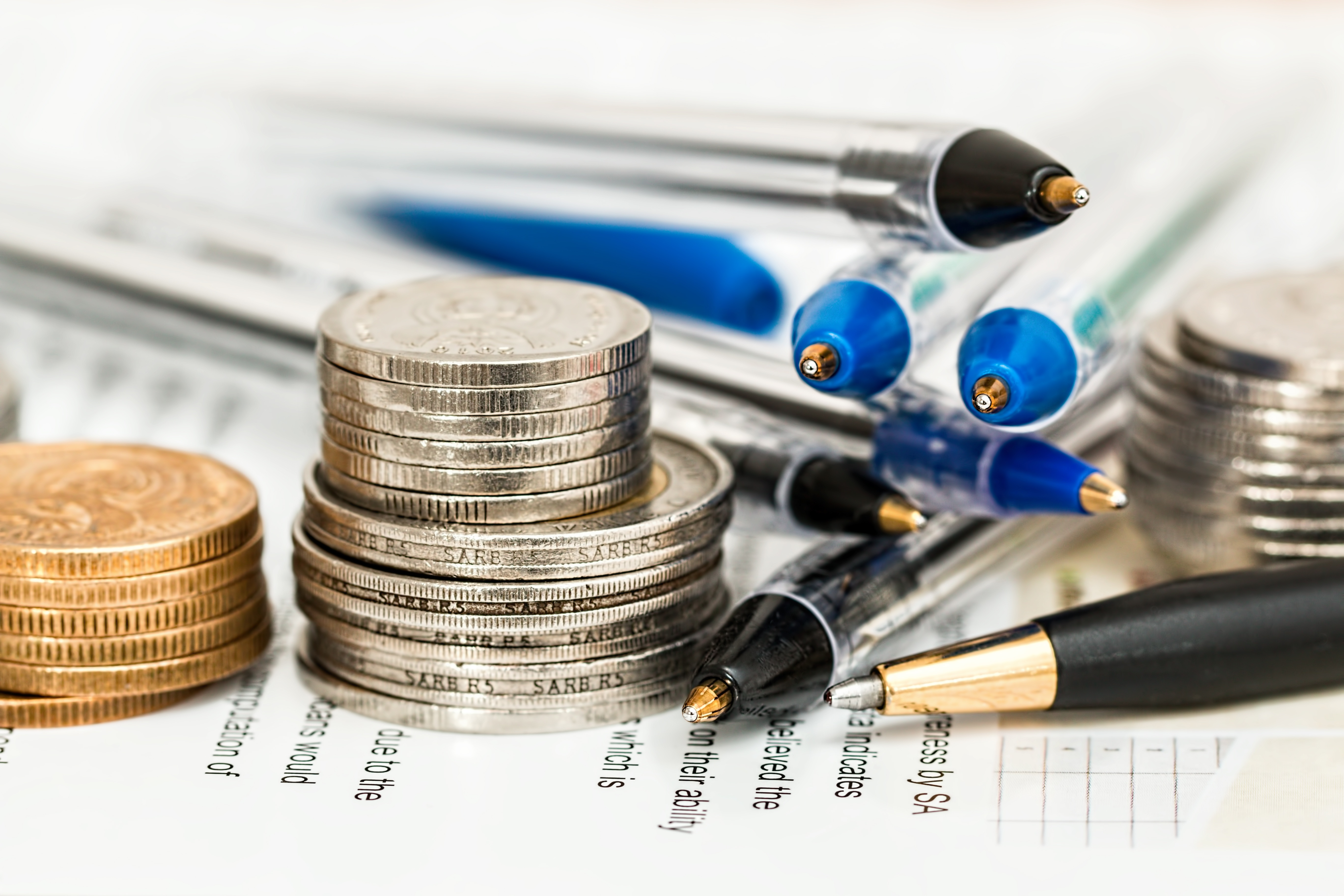 Tax credit or tax deduction? Which one is better for you? Coins stacked with piles of pens.